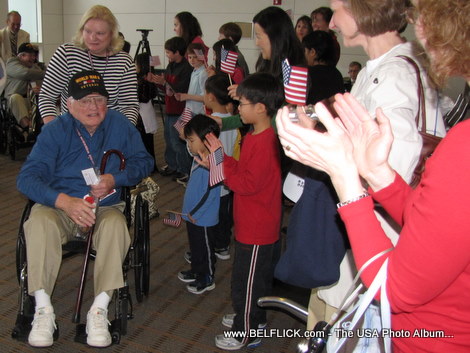 A World War II veteran sits on a wheelchair while an adoring crowd cheers for him